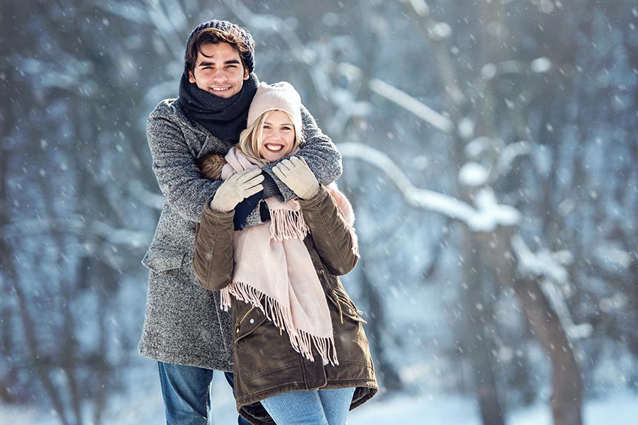 Personal Insurance - Couple Standing in the Snow in Front of Bare Trees, Smiling and Holding One Another